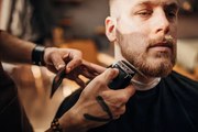 Fotografie Male barber cutting beard of client in barber shop, South_agency